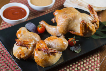 Grilled Chickens tobacco on the black plate with two sauces.