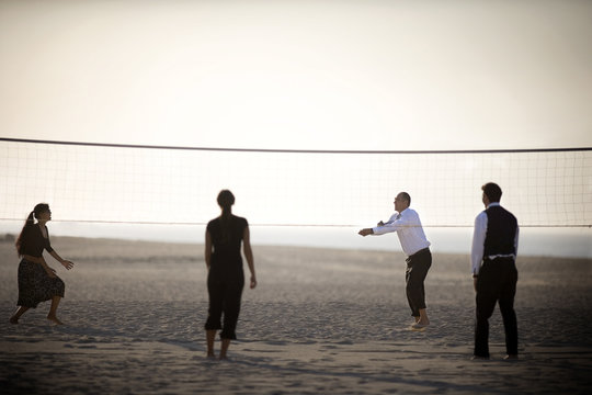 Two couples are playing volleyball on the beach.