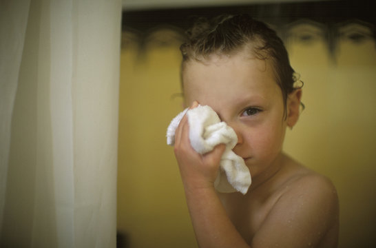 A small boy rubs his right eye with a towel.