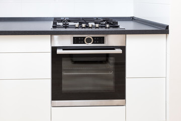 Build-on oven and hob in white kitchen with black counter, close up. 