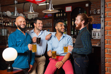 Fototapeta na wymiar Man Group In Bar Hold Glasses Talking, Drinking Beer Mugs, Mix Race Cheerful Friends Wear Shirts