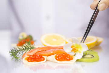 Tweezers in the hands of chef/The cook prepares food. Salmon, red caviar, kiwi, lemon.