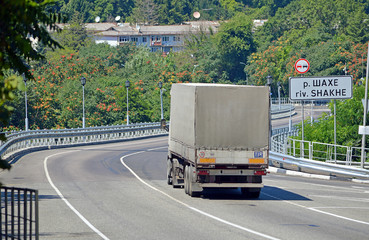Грузовик-фура движется по трассе перед мостом через реку Шахе