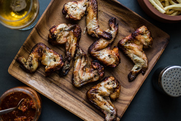 Chicken Wings in a wooden plate with potatoes, beverage and tomato sauce.