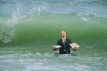 Businessman holding paperwork getting ready to be hit by a big wave representing drowning in...