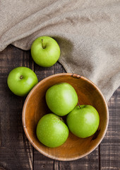 Green organic healthy apples in bowl on wooden board