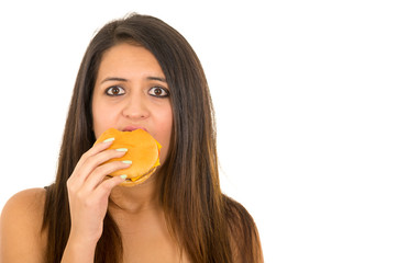 Portrait beautiful young woman posing for camera eating hamburger while making guilty facial expression, white studio background