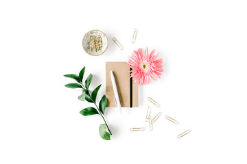 pink gerbera daisy, green branch, golden clips, craft diary and pen on white background. flat lay, top view