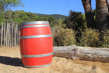 Obraz premium Bright red wooden barrel on a beach in tropical beach paradise with trees, log and rustic fence