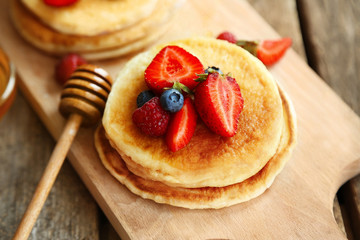 Tasty pancakes with berries and honey on cutting board