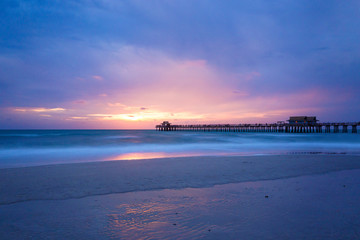 Obraz premium The sun goes down at the Naples Pier in the Gulf of Mexico, Southwest Florida, USA. Amazing landscape spot of the sun coming down at blue hour in this idyllic place for family vacation and relax.