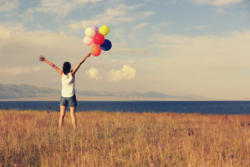 cheering young asian woman on sunset grassland with colored balloons