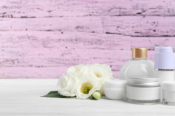 Different cosmetic bottles and eustoma flowers on purple wooden background