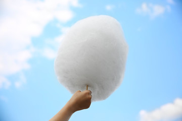 Female hand holding cotton candy on blue sky background