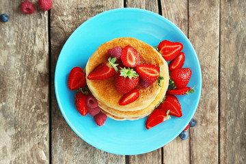 Tasty pancakes with fresh berries on plate on wooden background, top view