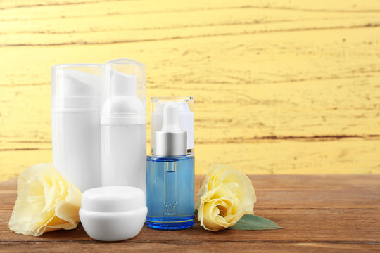 Different cosmetic bottles and eustoma flowers on yellow wall background
