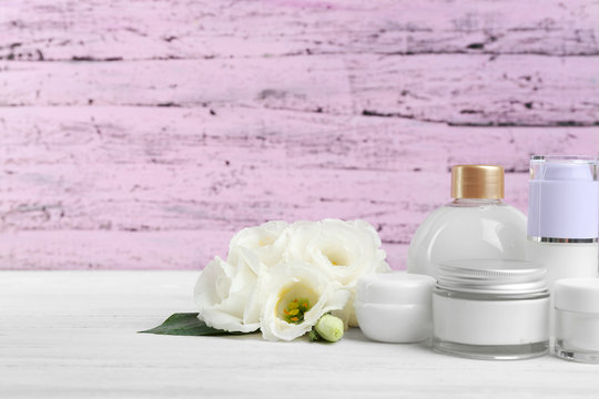 Different cosmetic bottles and eustoma flowers on purple wooden background
