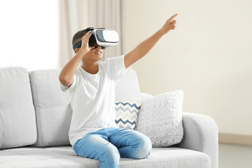 African-American boy wearing virtual reality glasses and sitting on sofa in a room