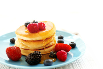 Delicious pancakes with berries and honey on blue plate