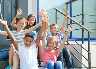 Fototapeta na wymiar Joyful schoolchildren with hands up sitting on school stair-steps