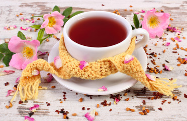 Cup of tea with wild rose flower on old rustic wooden background