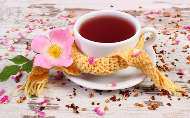 Cup of tea with wild rose flower on old rustic wooden background