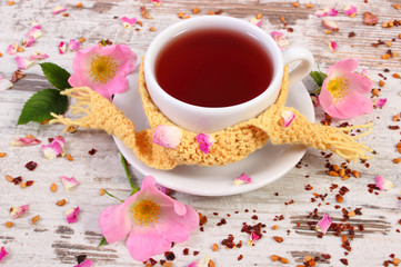 Cup of tea with wild rose flower on old rustic wooden background