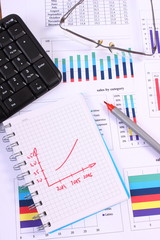 Pen, glasses and computer keyboard on financial graph, business concept
