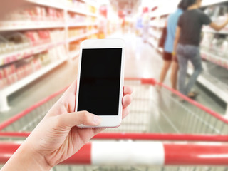 Female hand holding mobile smart phone on Supermarket blur backg