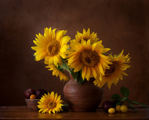 Bouquet of sunflowers in old clay jug. In the foreground branches with ripe cherry plum