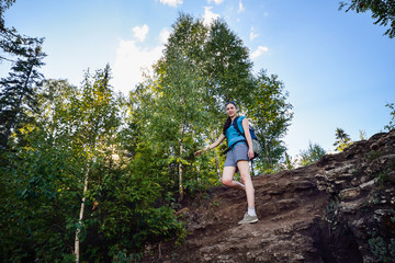 Hiker with backpack standing on top of rock and looking in camera  smiling