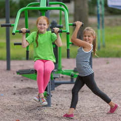 Fototapeta na wymiar Two little girls is engaged in fitness equipment outdoor..