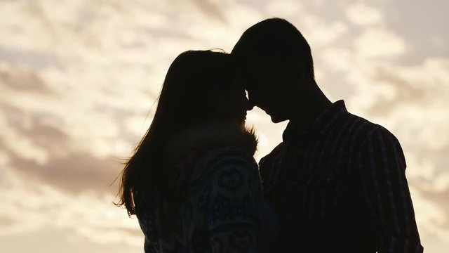 Silhouette of a young couple in love on the background of sky and sun, embrace, touch their foreheads