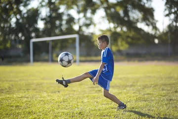 Foto op Plexiglas Boy kicking soccer ball on the football field © serbinov