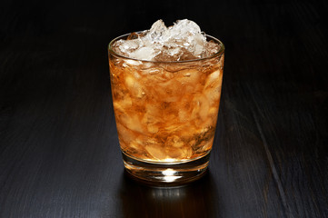Glass of whiskey with crushed ice on dark wooden background