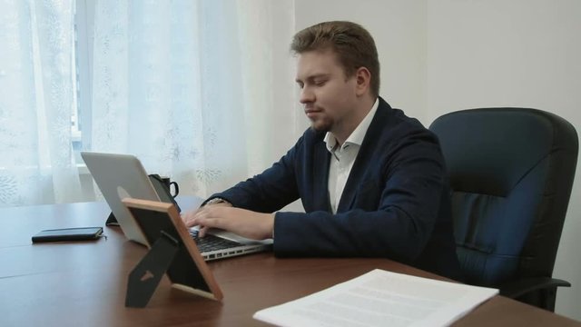 Young businessman working in his office in front of the laptop computer. Then looks at the picture of his family takes it, smiles and continues working