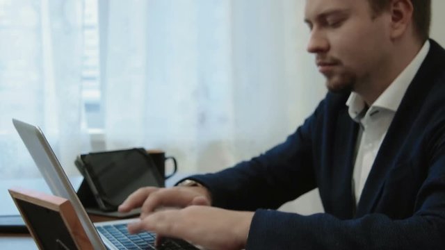Young businessman working in his office in front of the laptop computer. Then looks at the picture of his family takes it, smiles and continues working