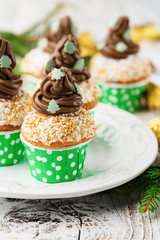 Christmas vanilla Cupcakes with chocolate buttercream icing and holiday decorations. White rustic wooden table, selective focus, celebration concept