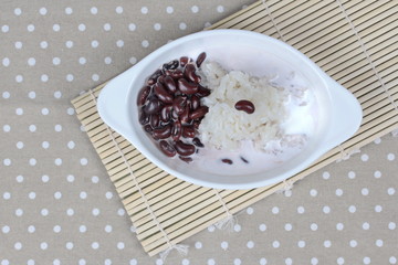 Black bean and sticky rice in sweet coconut cream topped coconut milk on black. Top view.
