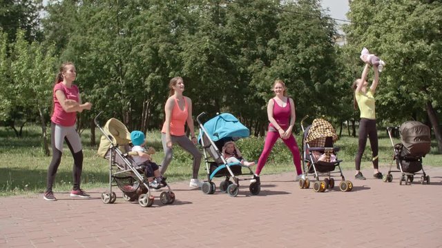 Group of sporty women exercising in the park while their babies sitting in strollers