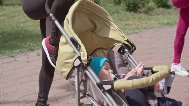 Young woman touching ground while bending with raised leg and pushing strollers with babies during exercising outdoors