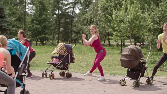 Group of women standing in front of their babies in strollers and doing side lunges with fitness instructor