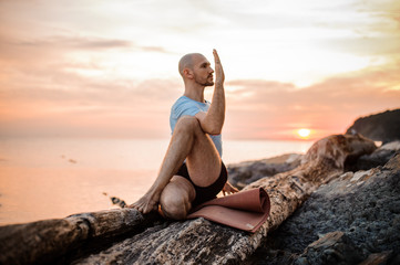 sitting man doing yoga on shore of ocean,