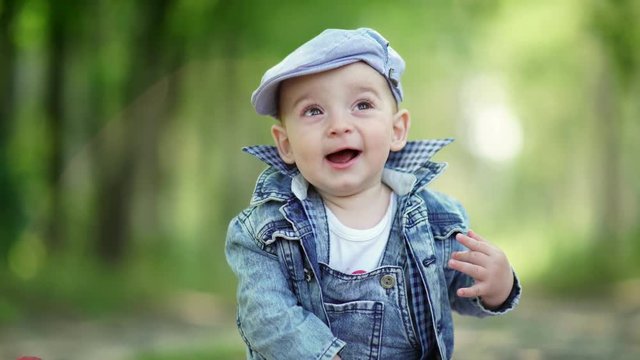 Little boy with apple. Toddler in denim suit and a cap holding apples in the hands. Basket with apples close. Joyful child in nature. A cute baby