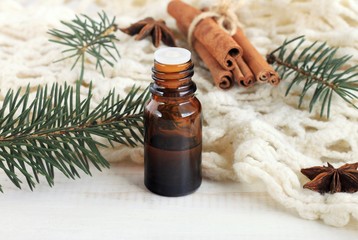 Essential pine or cinnamon oil. Winter fragrances. Glass dropper bottle of aroma oil, pine twigs, cinnamon, knitted plaid. 