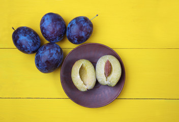 Plums on a yellow wooden table, plum cut in half lying on a plat