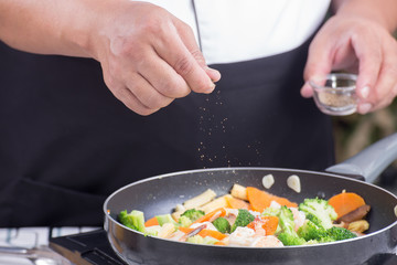 Chef putting Salt to the pan for cooking vegetable