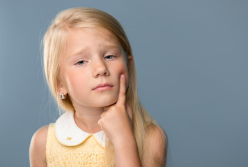 Portrait of a charming blonde little girl, points to a toothache