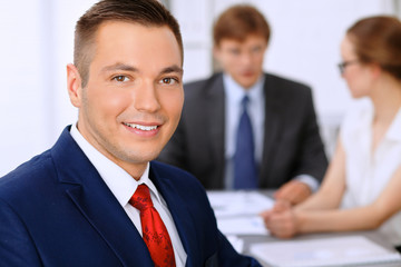 Portrait of cheerful smiling business man  against a group of business people at a meeting.