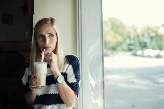 Portrait of young woman drinks coffee latte in cafe near the window